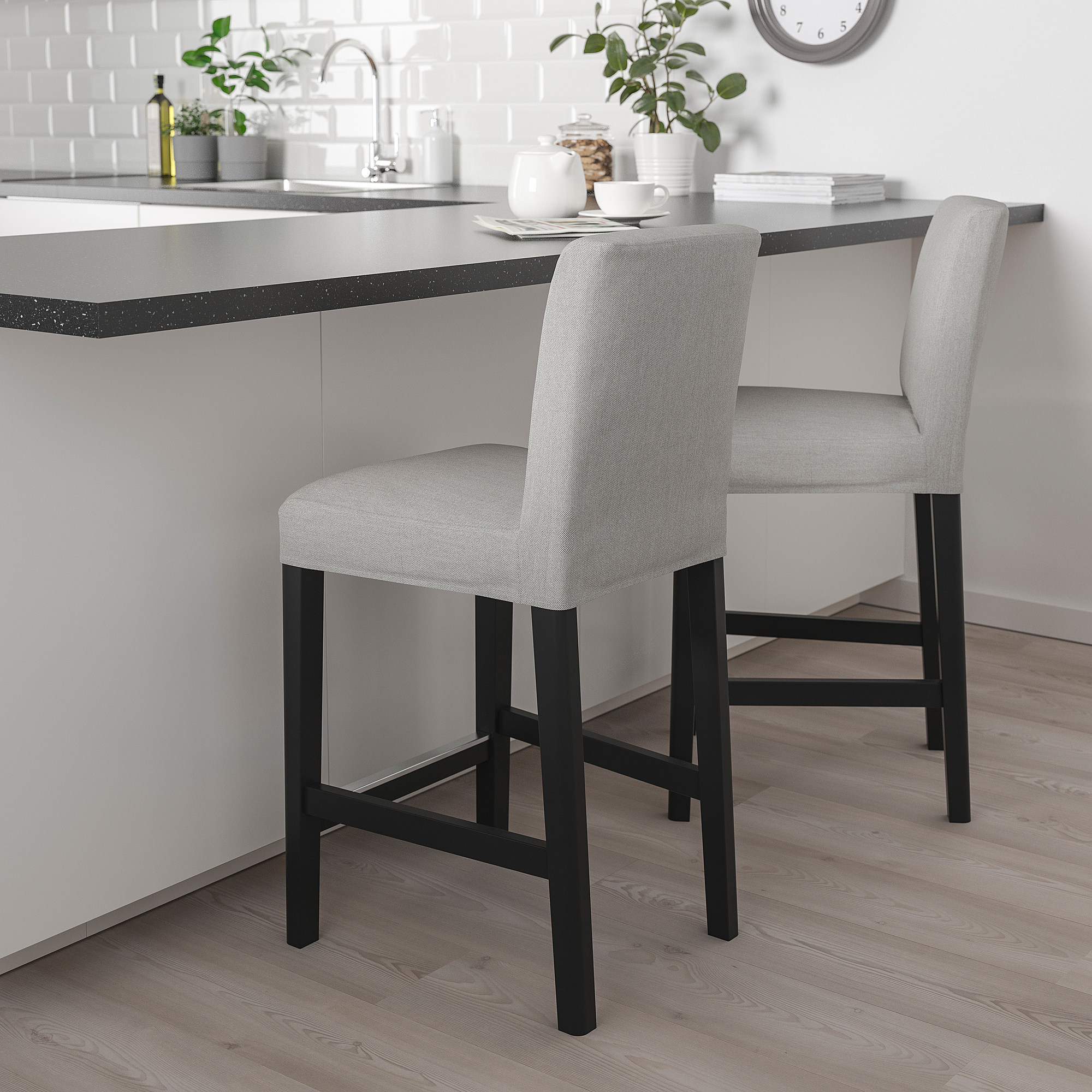 Modern kitchen with grey upholstered bar stools featuring black metal legs, positioned at a grey countertop with decorative items.