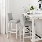 Two grey BERGMUND bar stools at white table, white room, minimalist design.