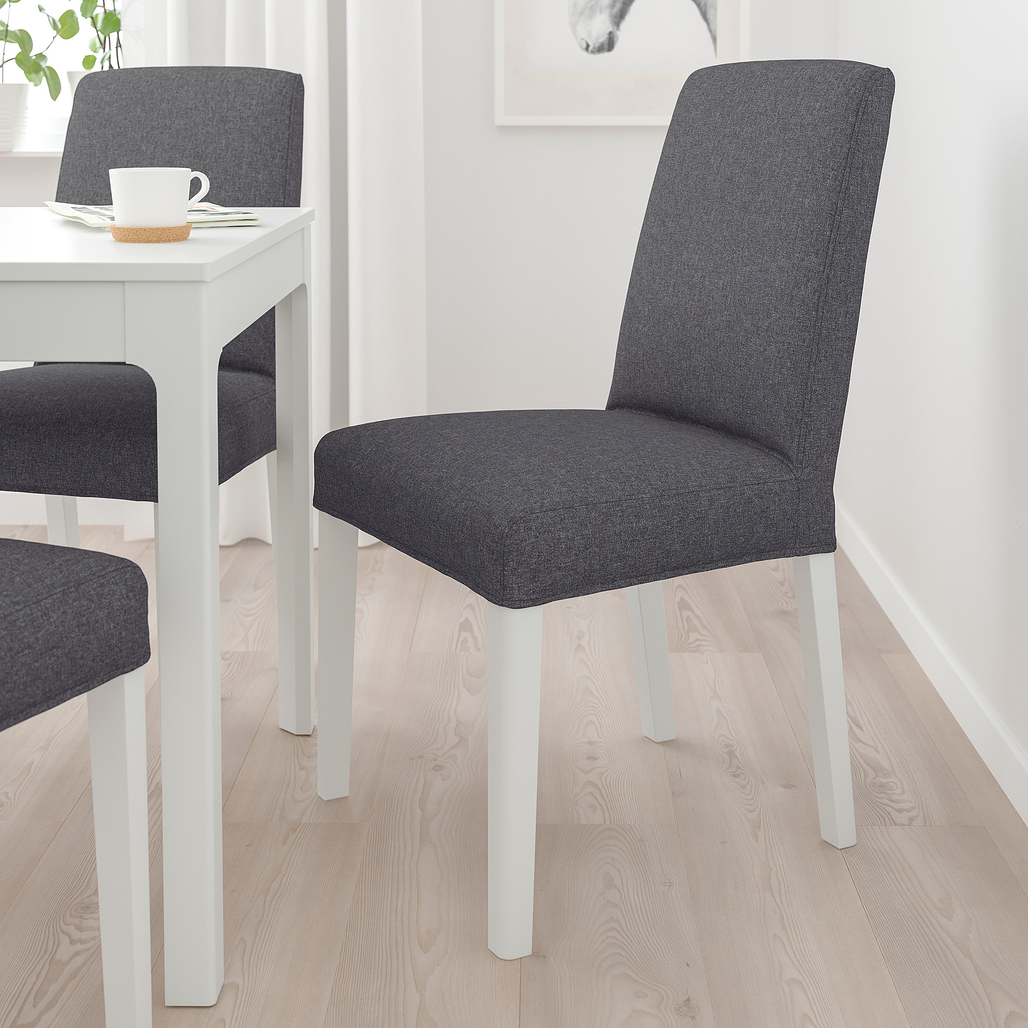 Modern grey fabric BERGMUND chairs with white legs and high backs beside a small white table, ideal for minimalist spaces.