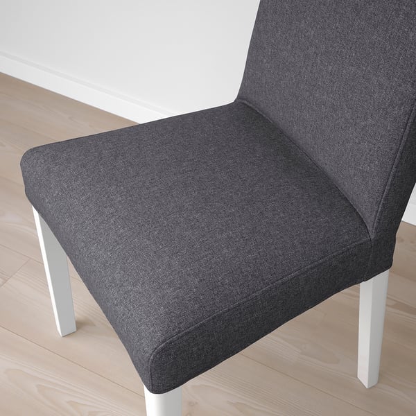 Grey upholstered chair with white legs on wooden floor. Modern, boxy design with high back.