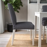 Dark grey upholstered chair with white legs near a small white table on a woven rug. The chair a high backrest and lumbar support for comfort.