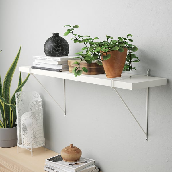 Shelf with vase, plant, books on gray wall.
