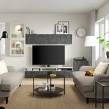 Modern living room with BERGSVIKEN tv stand, flat screen tv, gray sofas, colorful pillows, glass coffee table, and tall lamp.