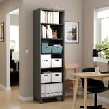 Black BESTÅ bookshelf with storage boxes and books, organized with decorative items, placed in a bright room with a chair nearby.
