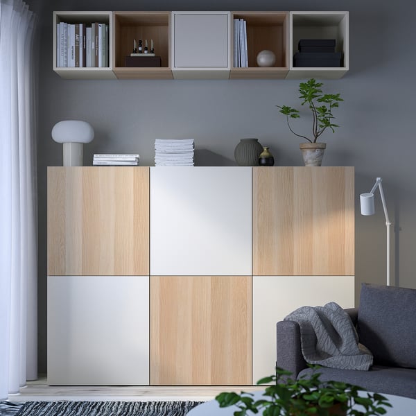 Modern living room with BESTÅ storage units. Shelves hold books, vases, and plants. Sofa, lamp, and rug complete the minimalist design.
