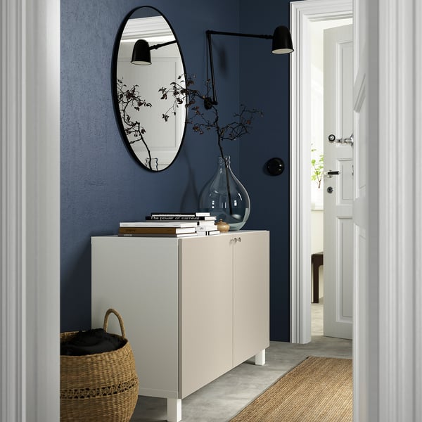 BESTÅ white sideboard with books & branches, mirror above, wicker basket beside.