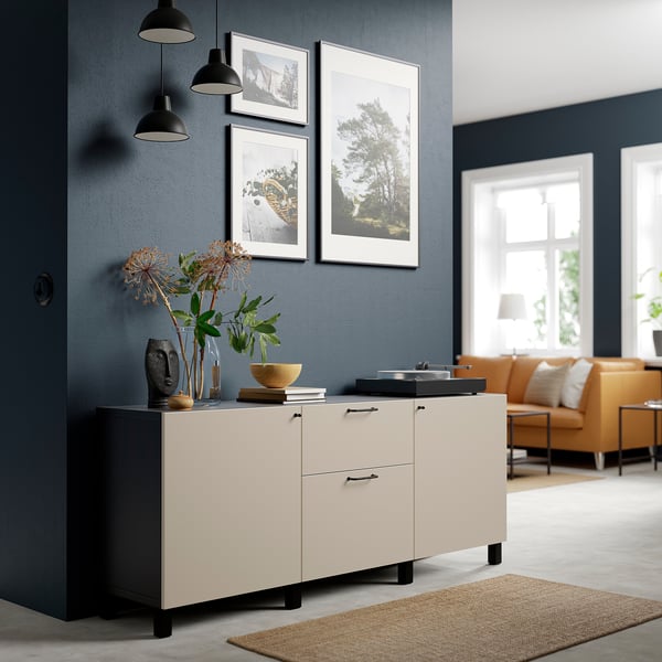 BESTÅ sideboard with vases, books. Orange chairs, lamp nearby. Dark blue wall, three framed pictures.