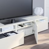 White tv stand with open drawers, holding gaming consoles, remote controls, and books.