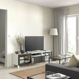 Modern living room with white BESTÅ tv bench, black tv, floor lamp, rug, and sofa near window with grey curtains.