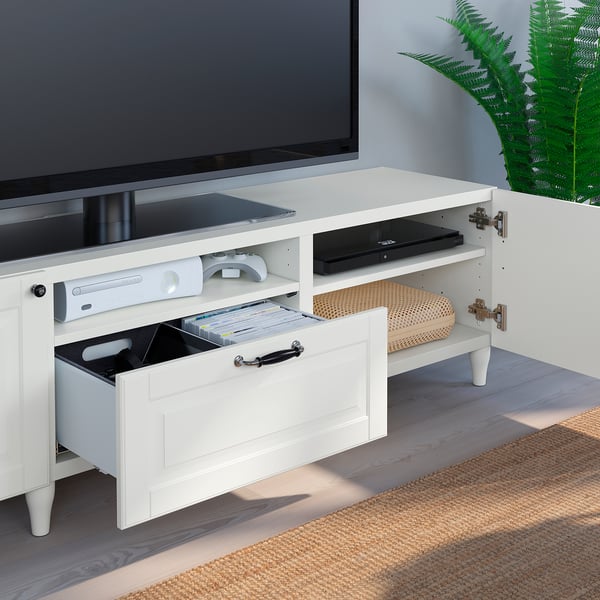 White tv stand with sliding drawer, holding gaming console, remote, and dvds. Stores and organises media devices and cables.