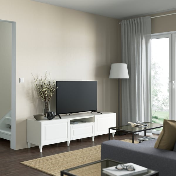 Modern living room with BESTÅ white tv stand. Black tv, vase with branches, grey curtains. Dark wood floor, light rug.