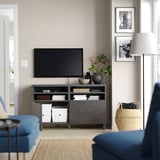 Modern living room with BESTÅ tv stand, blue couch, flat-screen tv, lamp, woven basket, and black & white photos.