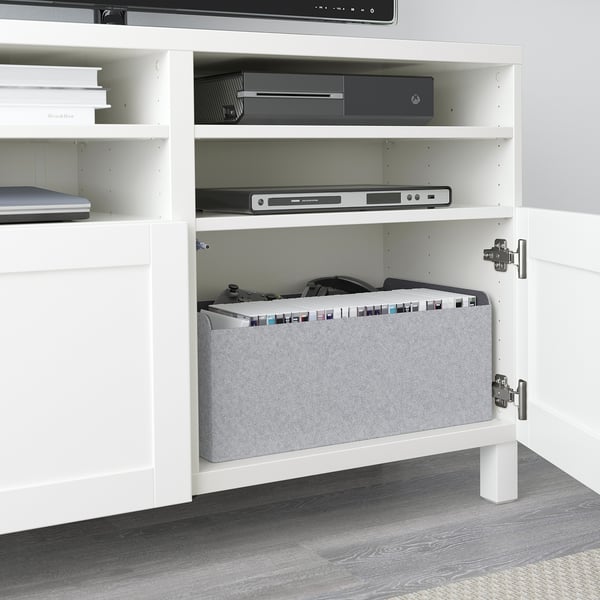 White BESTÅ tv unit with adjustable shelves, storing electronic devices and a felt organizer.