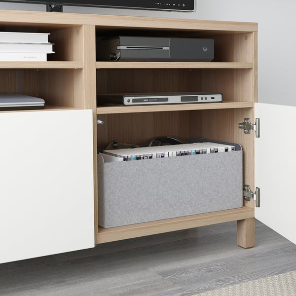 A wooden tv stand with open shelves, housing electronics and a laptop.