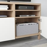 A wooden tv stand with open shelves, housing electronics and a laptop.