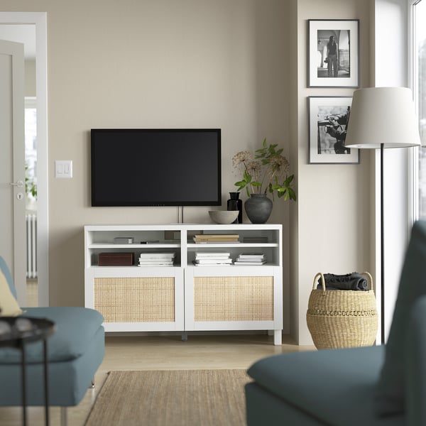 Modern living room with BESTÅ tv bench, flat-screen tv, books, decor, black-and-white photos, floor lamp, and blue seating.