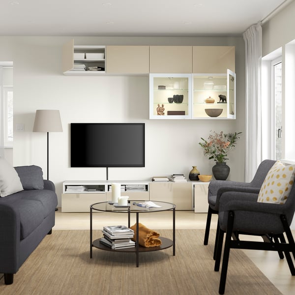 Modern living room with grey sofa, armchair, coffee table, flat screen tv on stand, and illuminated shelving unit.
