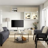 Modern living room with grey sofa, armchair, coffee table, flat screen tv on stand, and illuminated shelving unit.