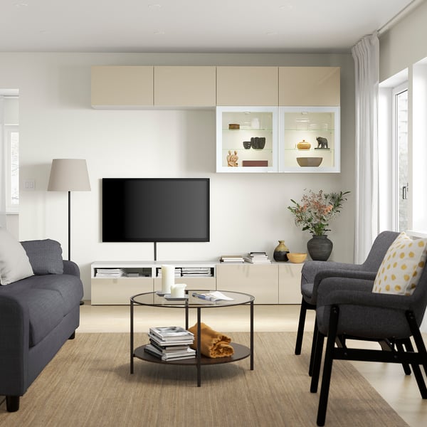 Modern living room with grey sofa, glass table, BESTÅ tv bench, beige cabinets, flat screen tv, and floral arrangement.