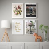 Wall gallery with floral prints and quote frame, beside a lamp and wooden horse on table.