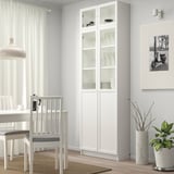 Minimalist white BILLY bookcase. Tall, sleek, glass doors, filled with plates.
