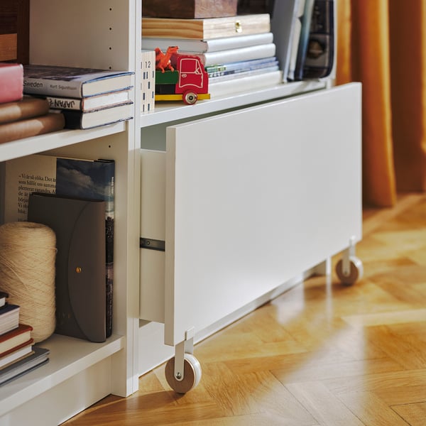 White BILLY bookcase with drawer on casters holds books and toys.