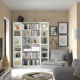 Modern living room with white BILLY bookcase, gray sofa, coffee table, and wooden walls. Decor includes books, vases, and framed art.