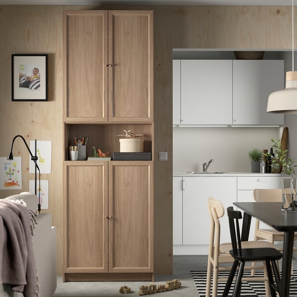 Modern living room with BILLY bookcase, decorative items, kitchen area, and warm wooden walls.
