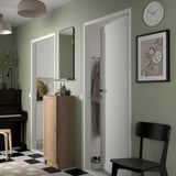 Stylish hallway with BILLY bookcase in natural wood against green wall, next to narrow white door.