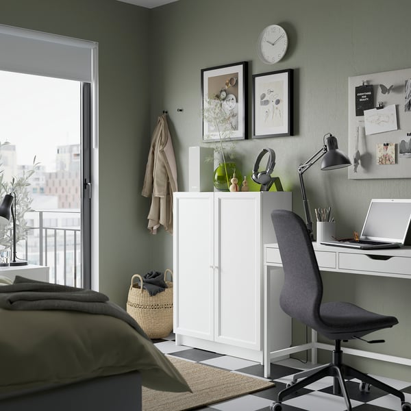Office corner in bedroom: grey chair, white desk, BILLY bookcase, green wall, balcony view, decorations.