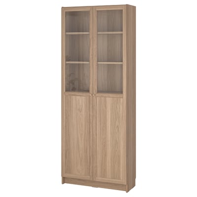 A BILLY bookcase in oak color with glass doors. The design is simple and versatile for various uses.