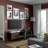 Modern living room with dark oak veneer cabinet, flat-screen tv, framed photos, lamp, and glass coffee table by window.
