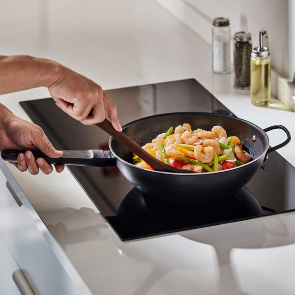 Person cooks shrimp and vegetable stir-fry in BLÅGYLTA wok. Woks non-stick coating ensures even heat distribution and easy cleaning.