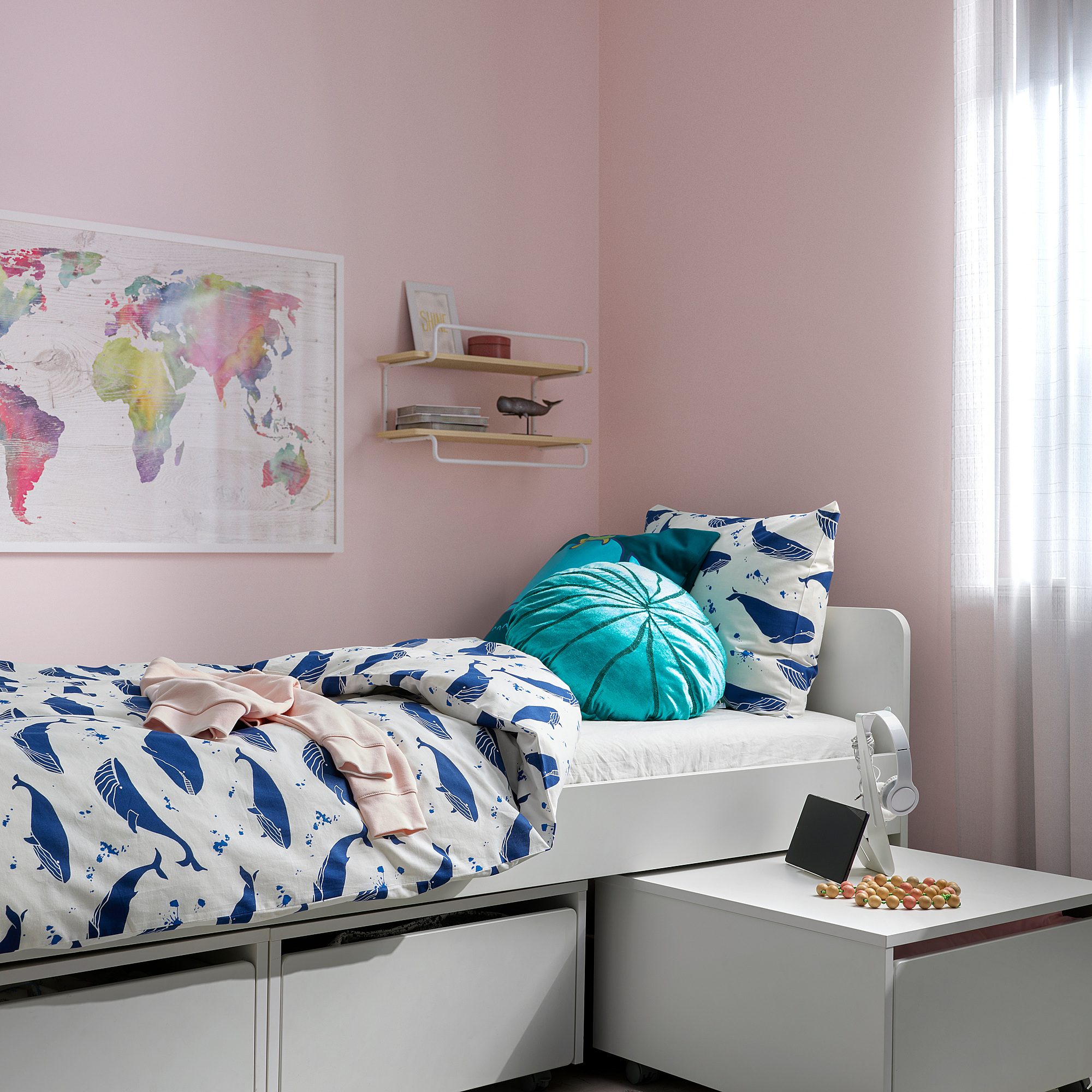A cozy bedroom with a BLÅVINGAD duvet cover in blue whale design on a bed, featuring a turquoise pillow and a colorful world map on the wall.