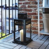 Black metal lantern with candle on tiled balcony, providing a warm ambiance.