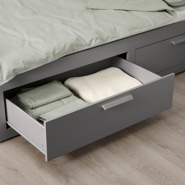 An open gray drawer from a BRIMNES day-bed, storing folded bed linens.