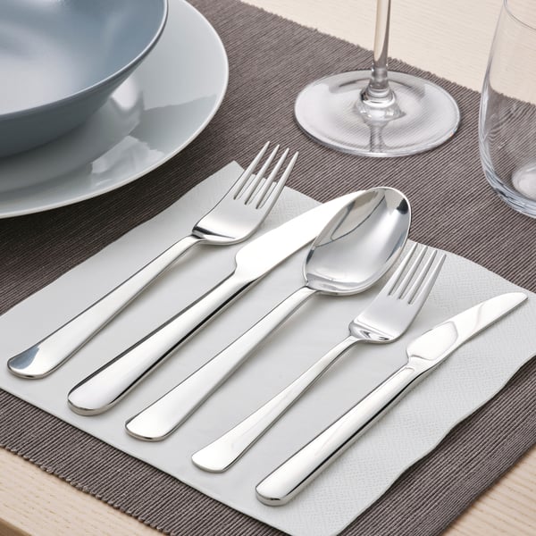Silverware set on table: knife, fork, spoon, plate, glass, napkin.
