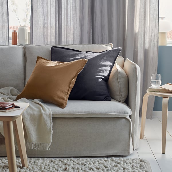 Modern living room with large light gray sofa, brown and gray pillows, wooden side tables, and white rug.