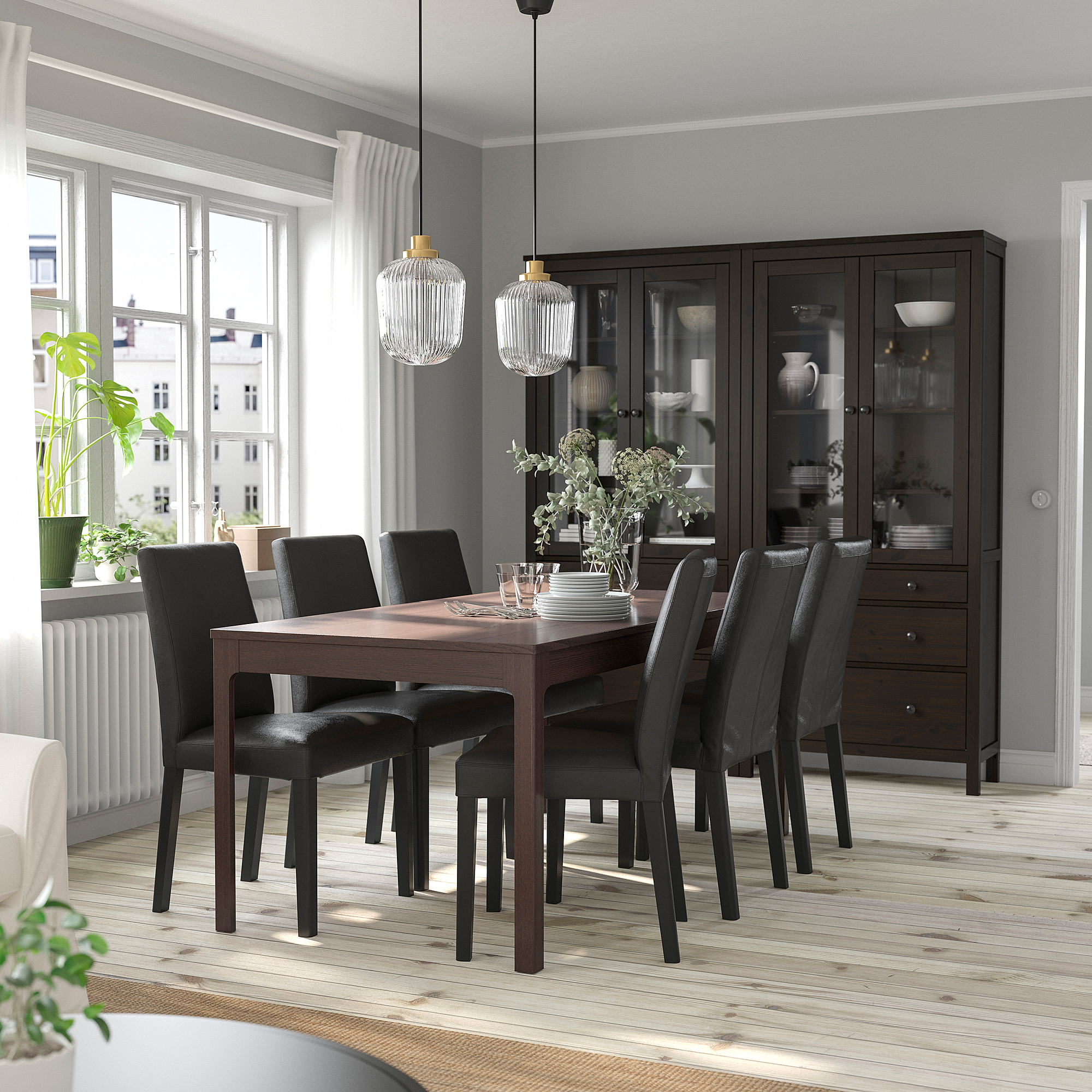 Modern dining setup with dark brown extendable table, six black chairs, wooden floor. Large window, hanging lights, and cabinet.