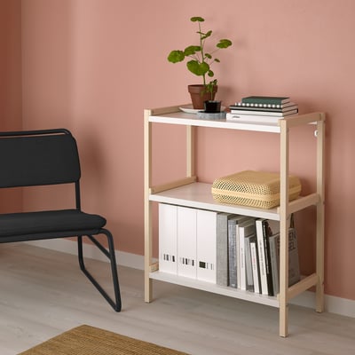Small, beige EKENABBEN shelf holds books & decor next to black chair.