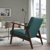 Teal upholstered retro-style armchair with wooden legs sits by a window in a cozy living room.