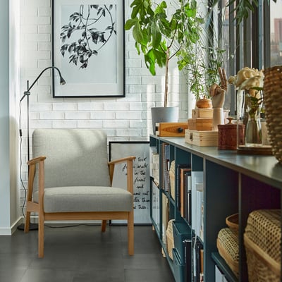 Gray EKENÄSET armchair against white wall with bookshelf, lamp, and plant.