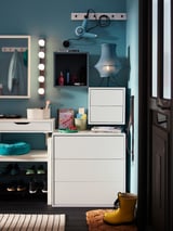 Well-organized teal entryway with white storage units featuring multiple compartments, a mirror with lights, and yellow rain boots.