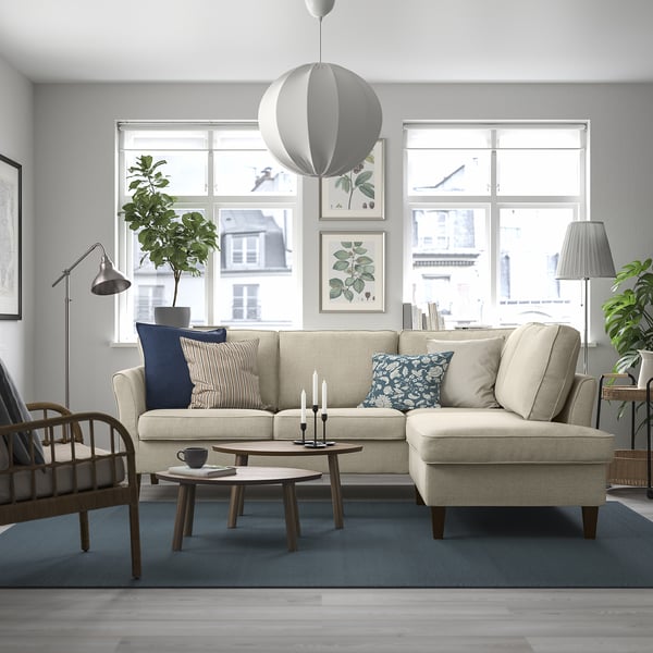 Modern living room with EKHOLMA sofa, armchair, coffee tables, blue rug, and hanging lamp. Large windows, plants, and wall art. Sofa as focal point.