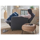 Relaxing in a grey EKOLSUND recliner, feet up on a wicker stool, surrounded by home decor.