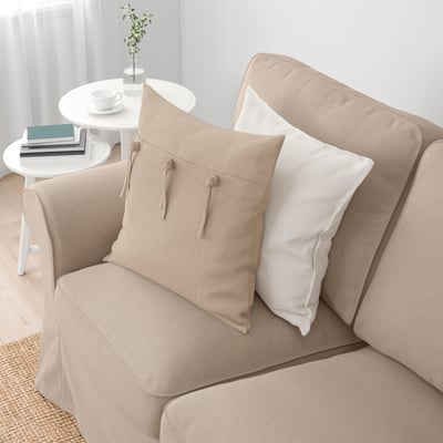 A beige EKTORP sofa with cushions, including a beige pillow with ties and a white pillow, set in a cozy room with a side table and decor.