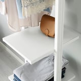 Closet with white ELVARLI shelves, a tan leather purse, and folded clothes in light grey.