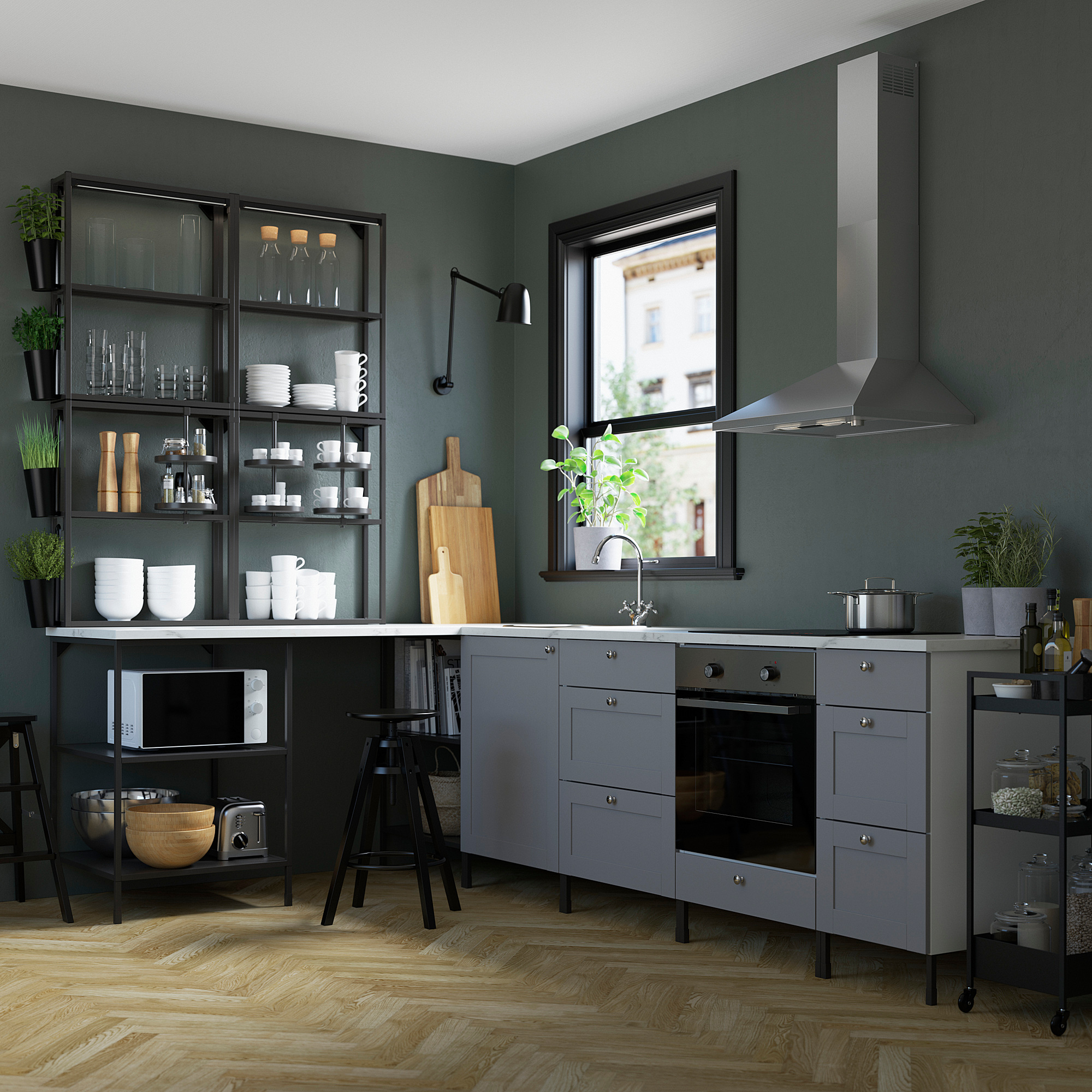 Modern kitchen with gray cabinets, stainless steel appliances, wood floor, white dishes, plants, green walls, window.