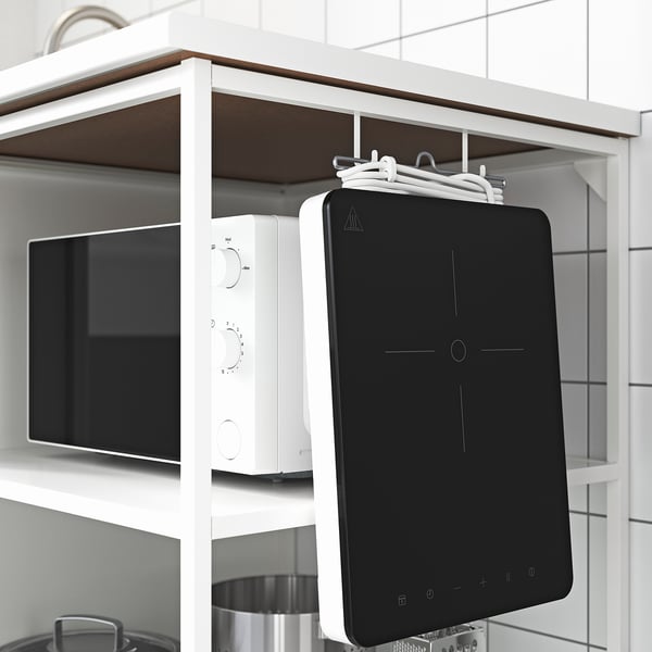 Modern kitchen setup featuring a white microwave, black tablet-sized device, and metal pots on a white shelf unit.