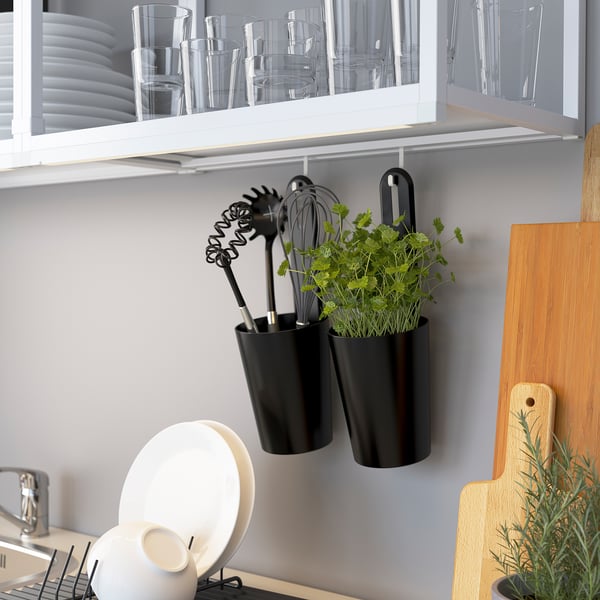 Wall-mounted kitchen storage holding cups, utensils, and plants.